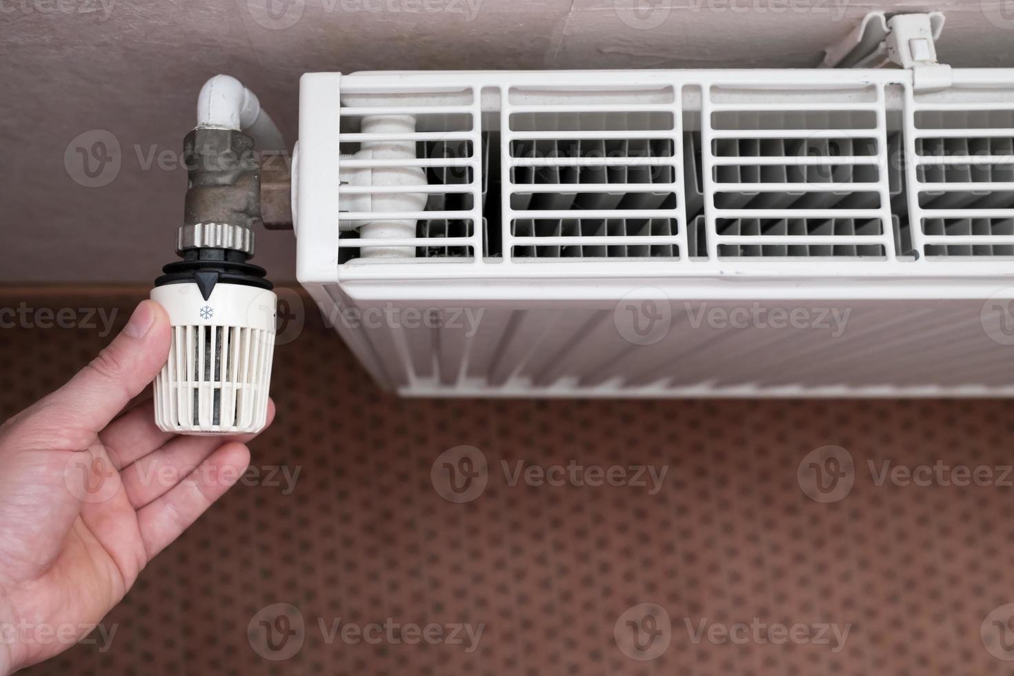 Hand turns the radiator thermostat to the minimum due to rising gas prices. Concept of energy crisis and savings. Top view. photo