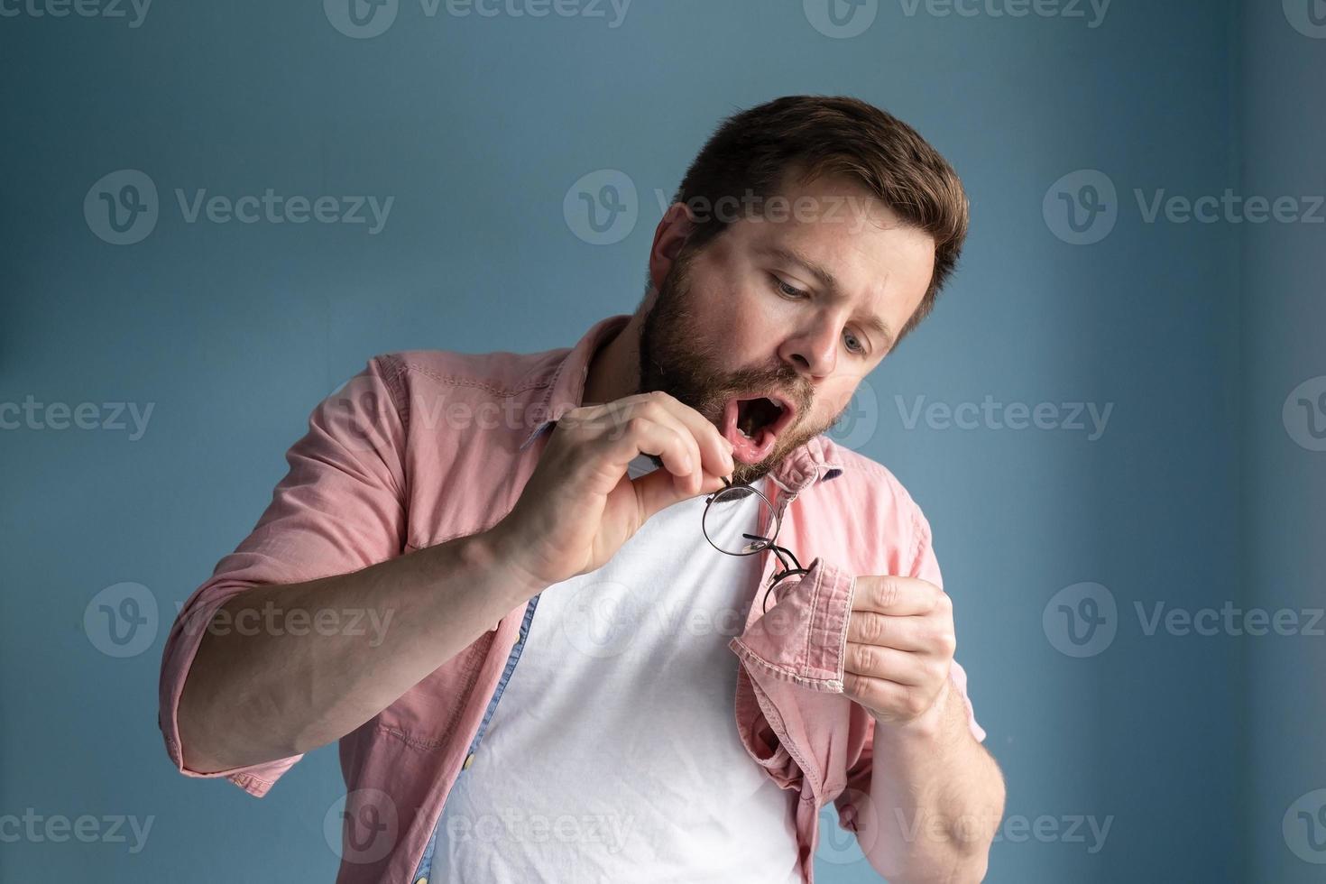 Concentrated man breathes on the lenses of his glasses and wipes them from dirt and dust with shirt. photo