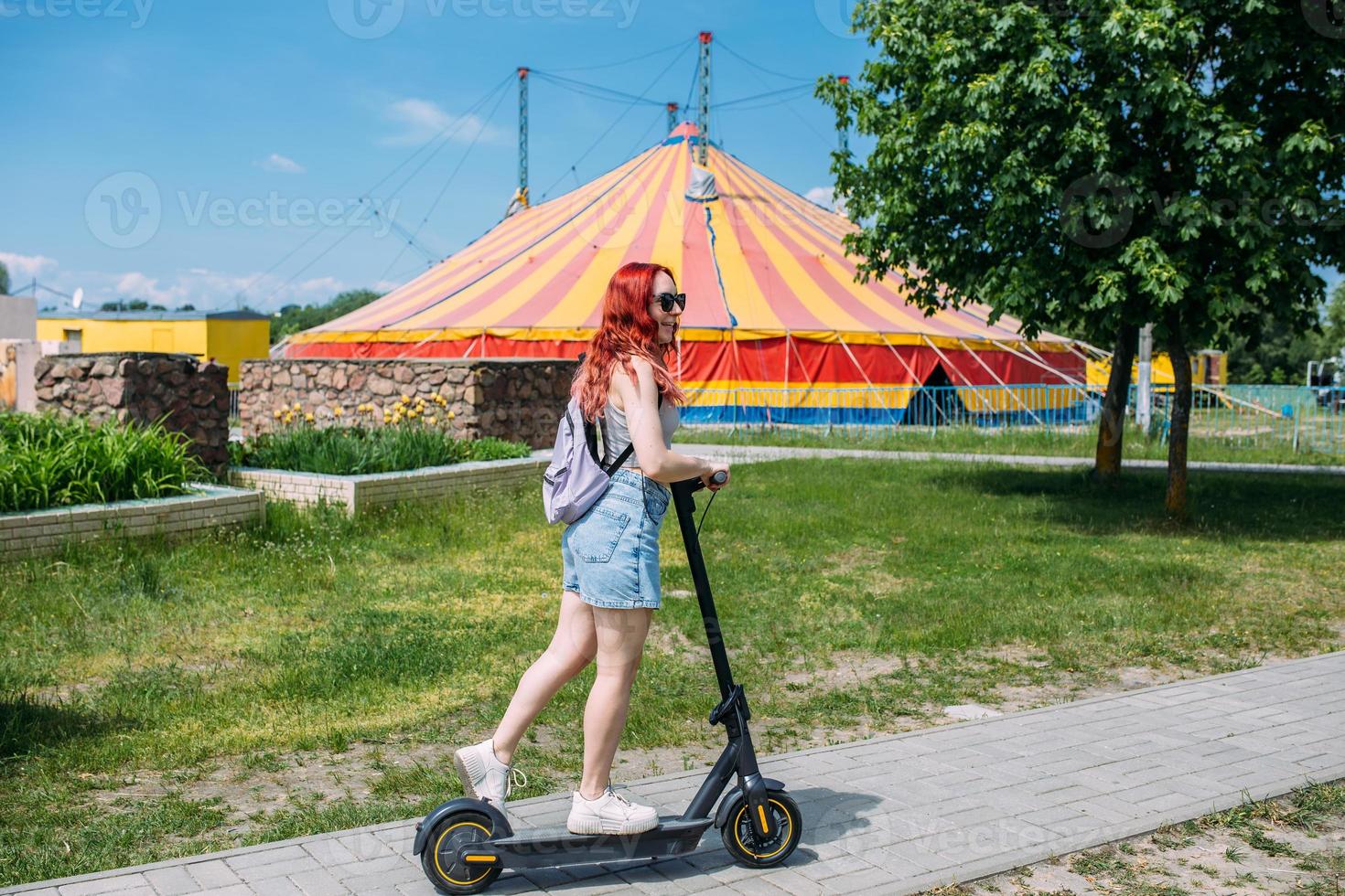 Young bright woman smiles and rides electric scooter in the summer in the city photo