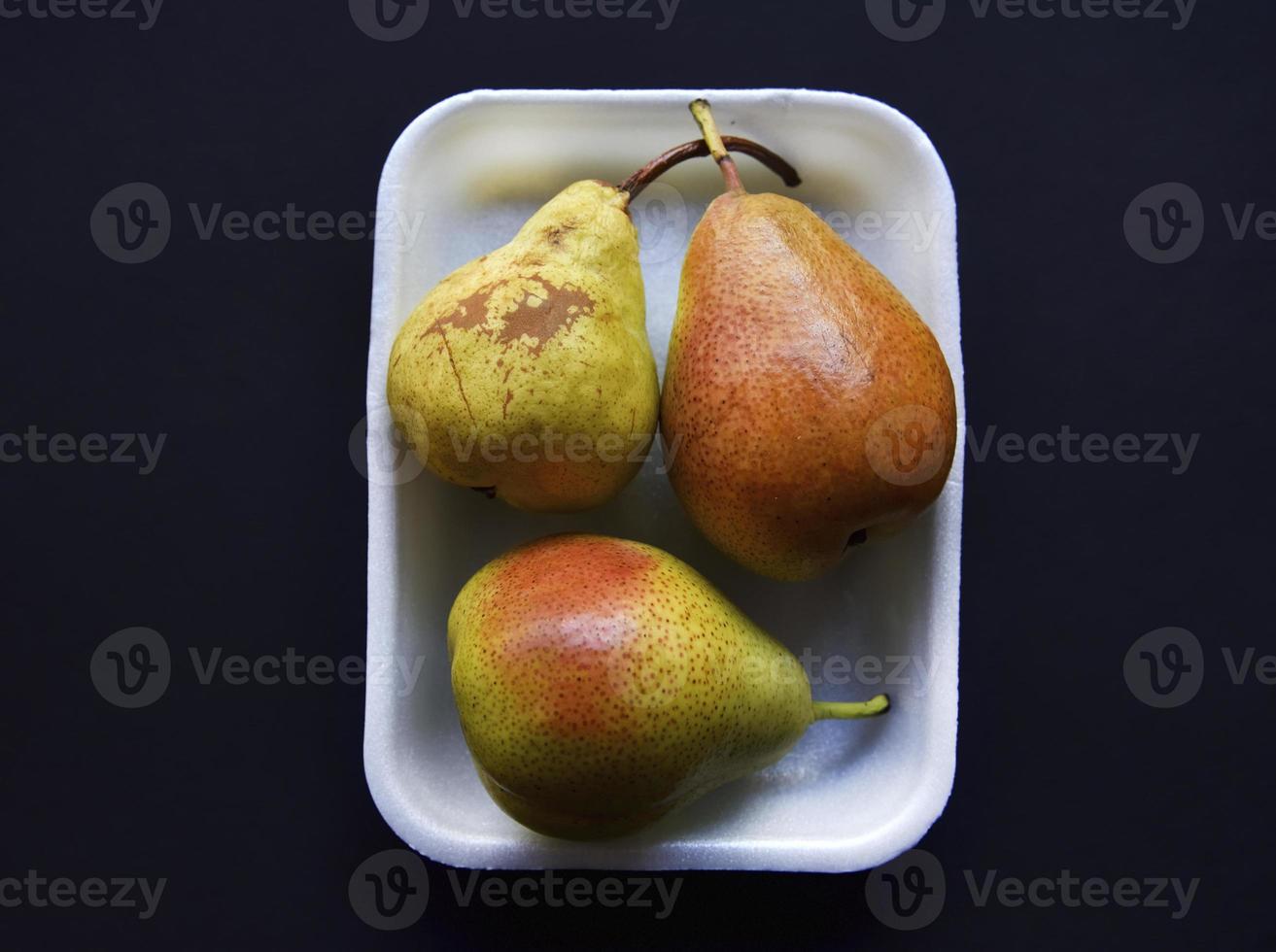 Red and green pears on a black background. Pears in a package from the store. Beautiful fruits of pears. photo