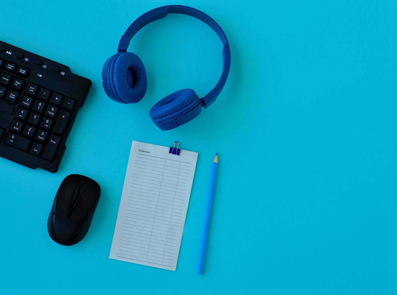 Flat lay home office desk. Workspace with laptop, headphones, pencil, alarm clock and a piece of paper for notes on blue background. Top view feminine background. photo