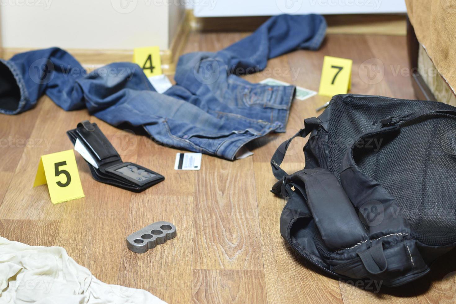 Crime scene investigation - numbering of evidences after the murdering in apartment. Brass knuckle, wallet and clothes with evidence markers photo