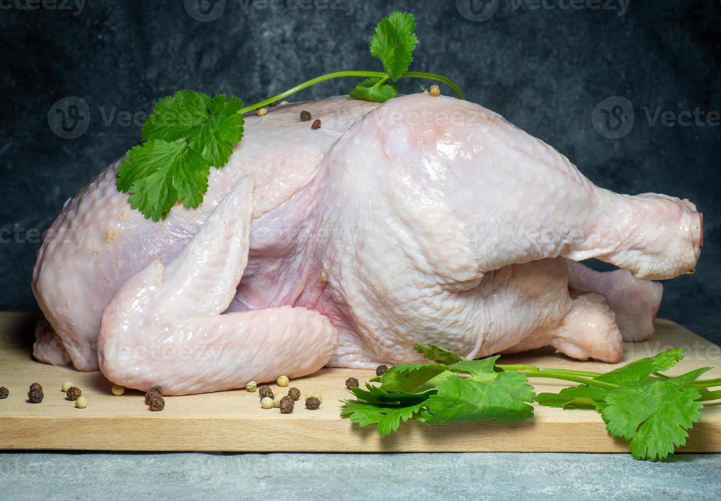 Raw whole chicken on a cutting board on a dark background. Food preparation. Cilantro and peppercorns.  Chicken in spices. Healthy food photo