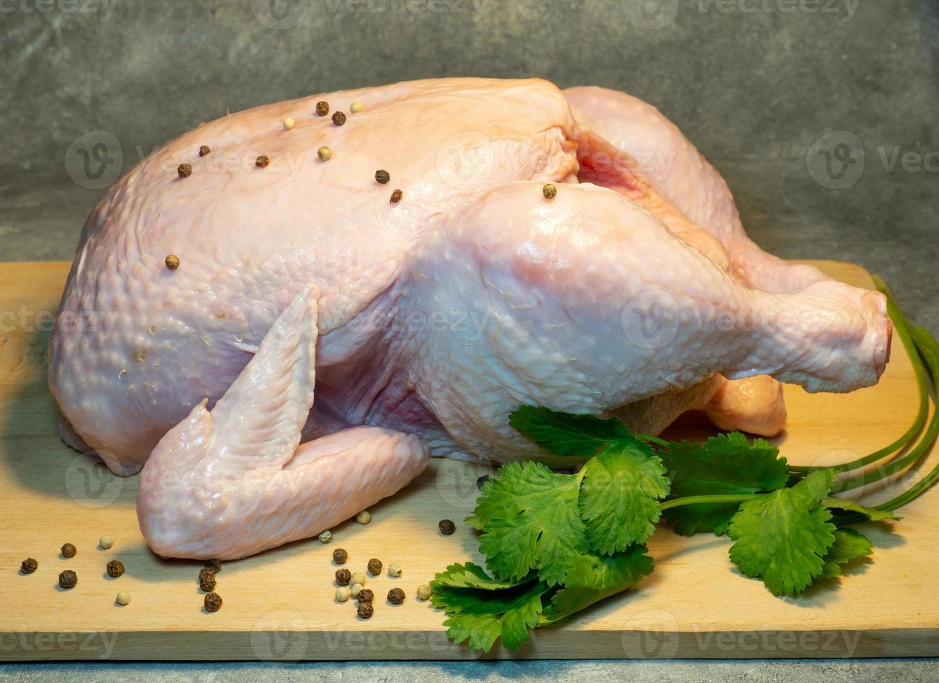 pollo entero crudo en una tabla de cortar sobre un fondo oscuro. preparación de comida. cilantro y granos de pimienta. pollo en especias. comida sana foto