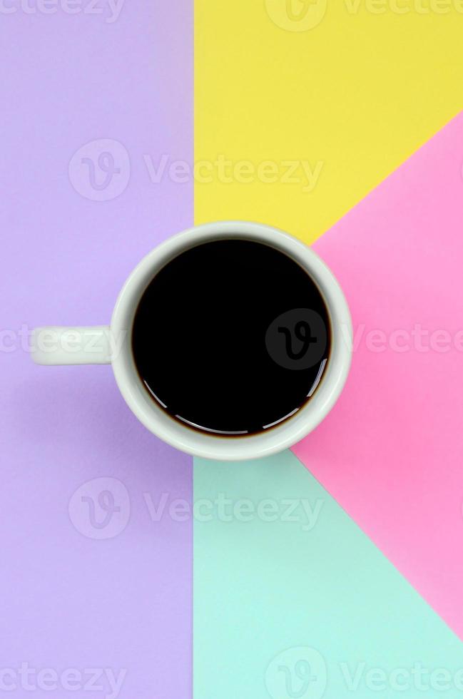 Small white coffee cup on texture background of fashion pastel blue, yellow, violet and pink colors paper in minimal concept photo