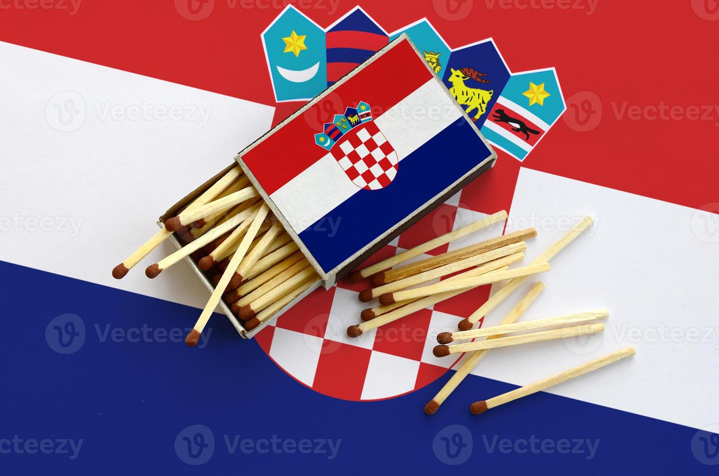 Croatia flag is shown on an open matchbox, from which several matches fall and lies on a large flag photo