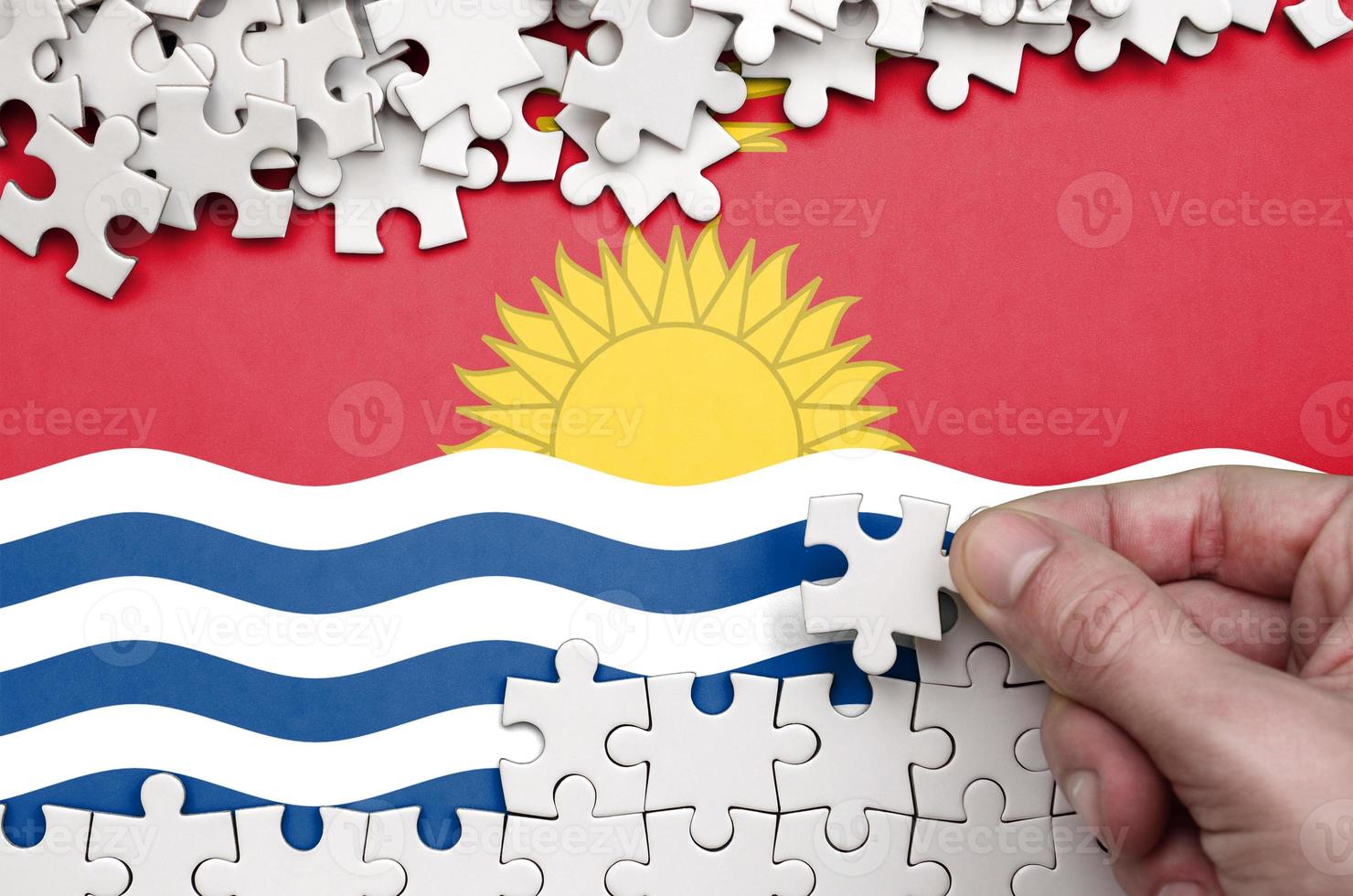 Kiribati flag is depicted on a table on which the human hand folds a puzzle of white color photo