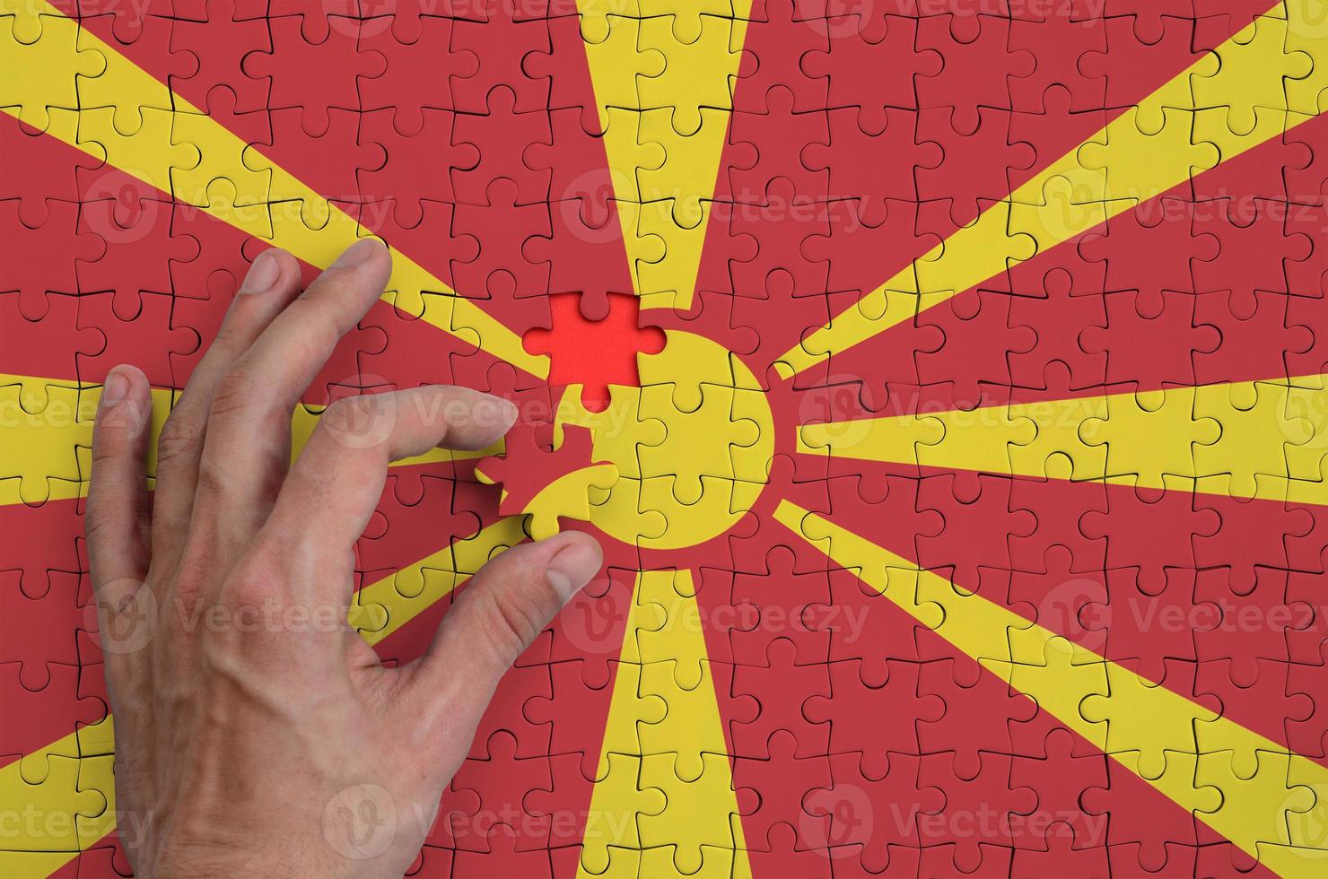 Macedonia flag is depicted on a puzzle, which the man's hand completes to fold photo