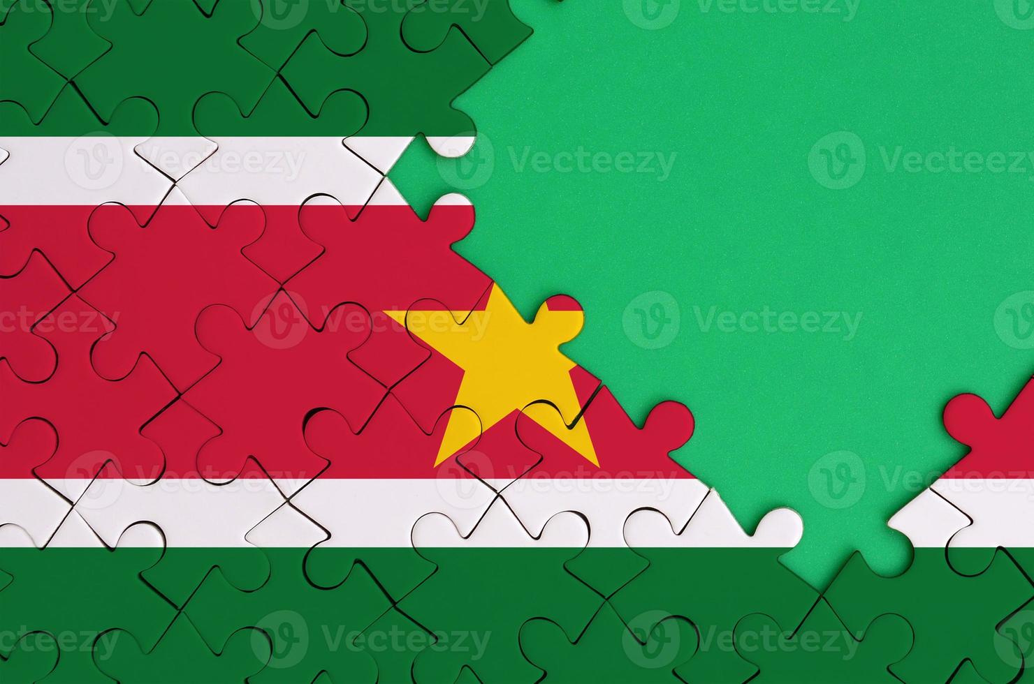 Suriname flag is depicted on a completed jigsaw puzzle with free green copy space on the right side photo