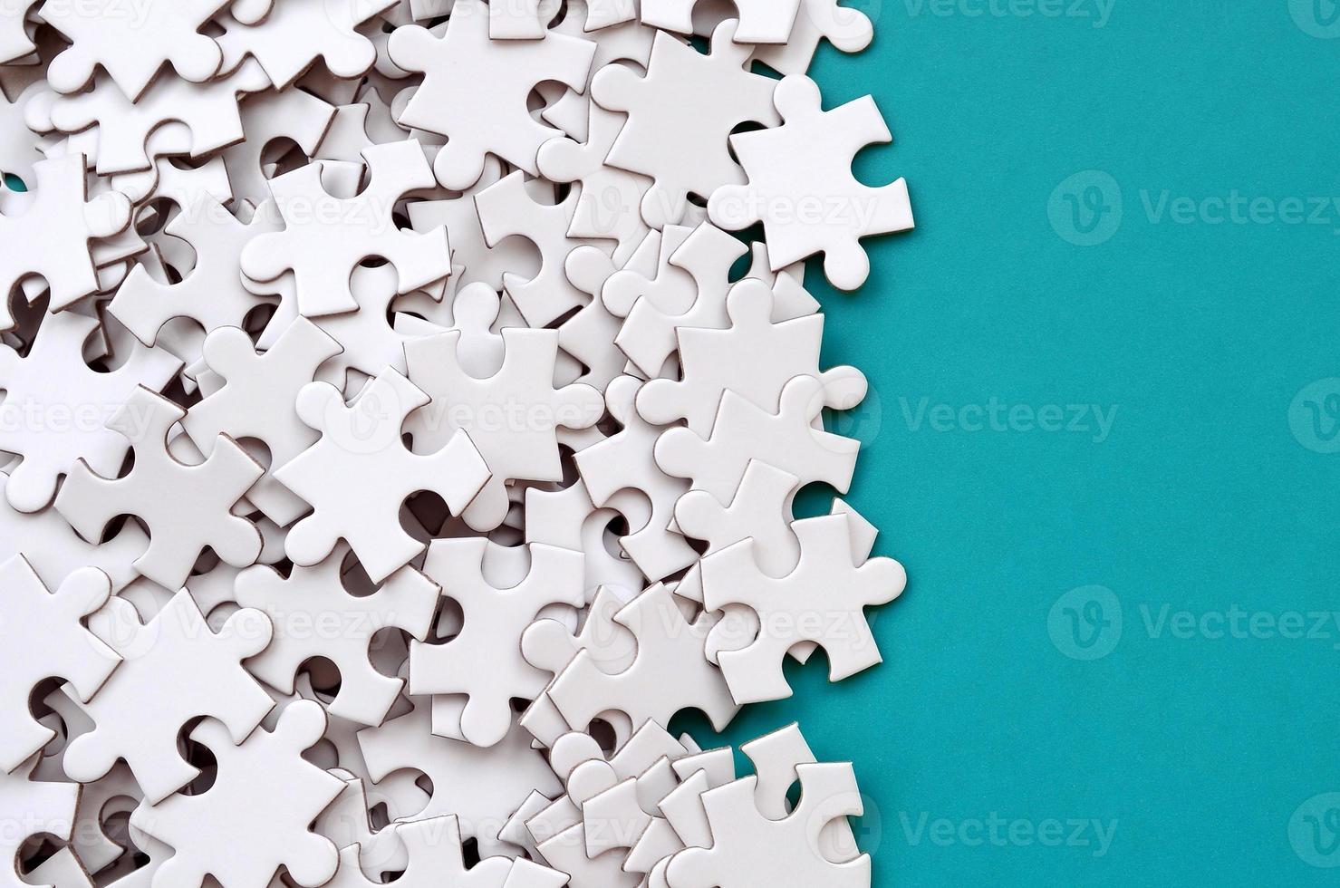 A pile of uncombed elements of a white jigsaw puzzle lies on the background of a blue surface. Texture photo with copy space for text