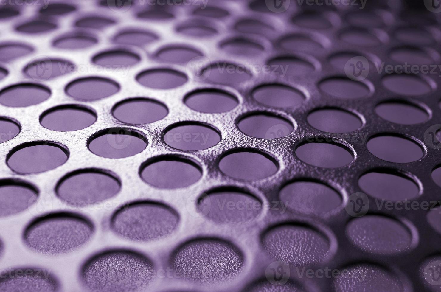 Black metal computer case panel mesh with holes on purple background. Abstract close up photo