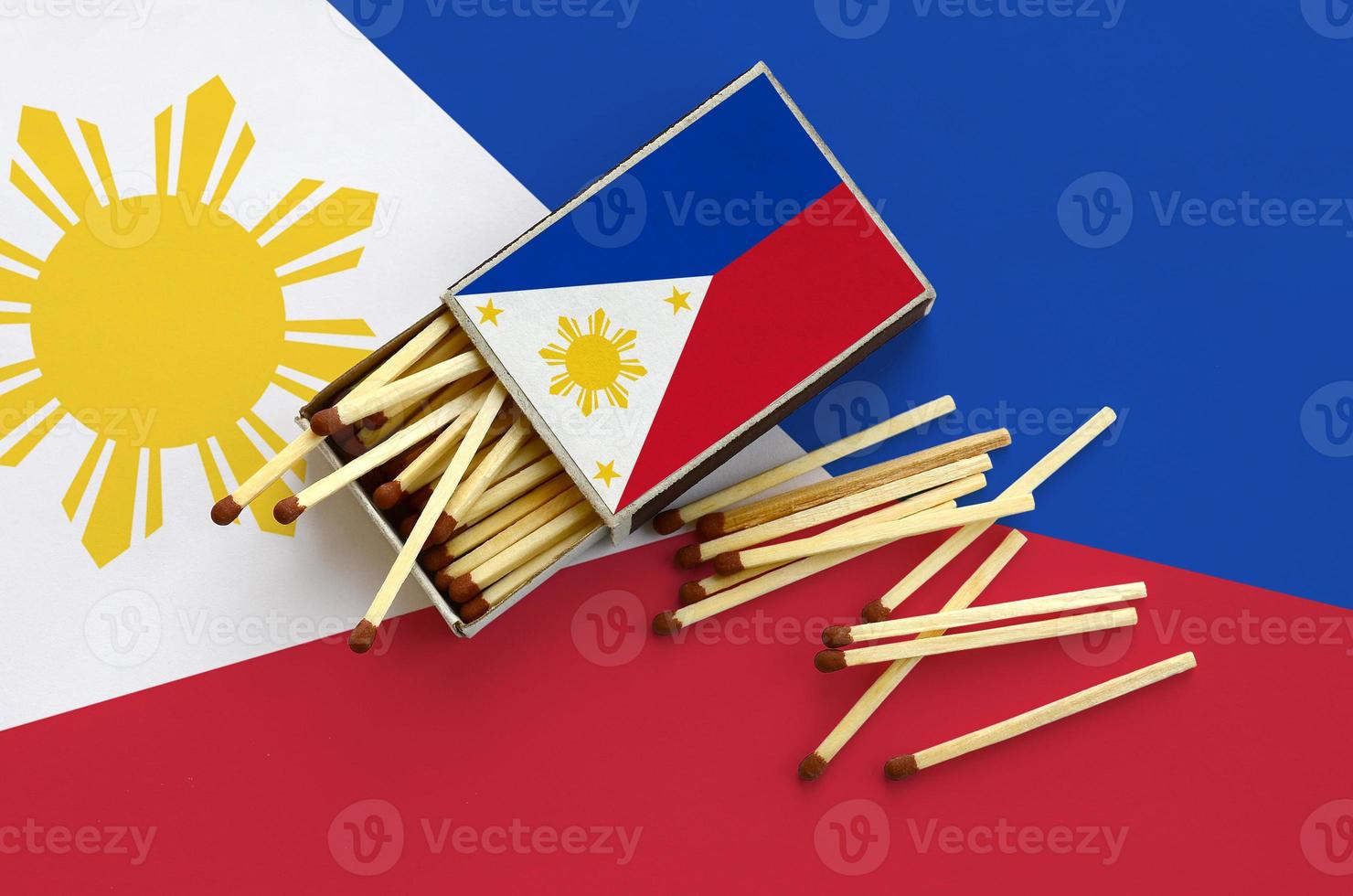 Philippines flag is shown on an open matchbox, from which several matches fall and lies on a large flag photo