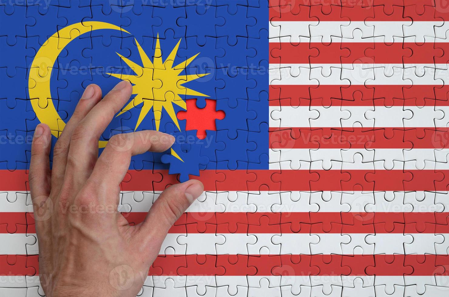 Malaysia flag is depicted on a puzzle, which the man's hand completes to fold photo