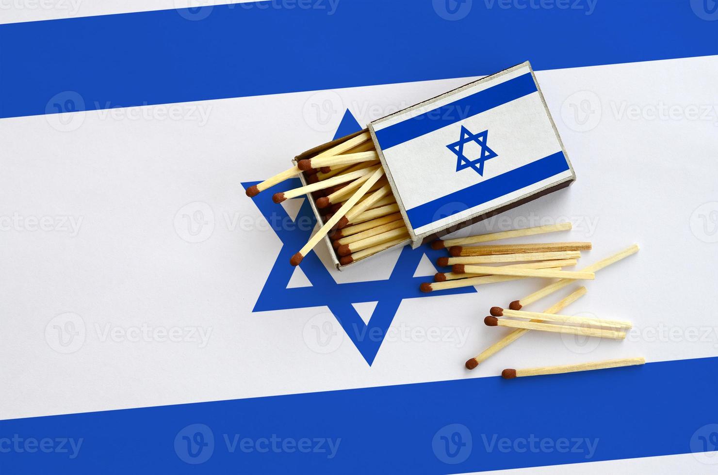 Israel flag is shown on an open matchbox, from which several matches fall and lies on a large flag photo