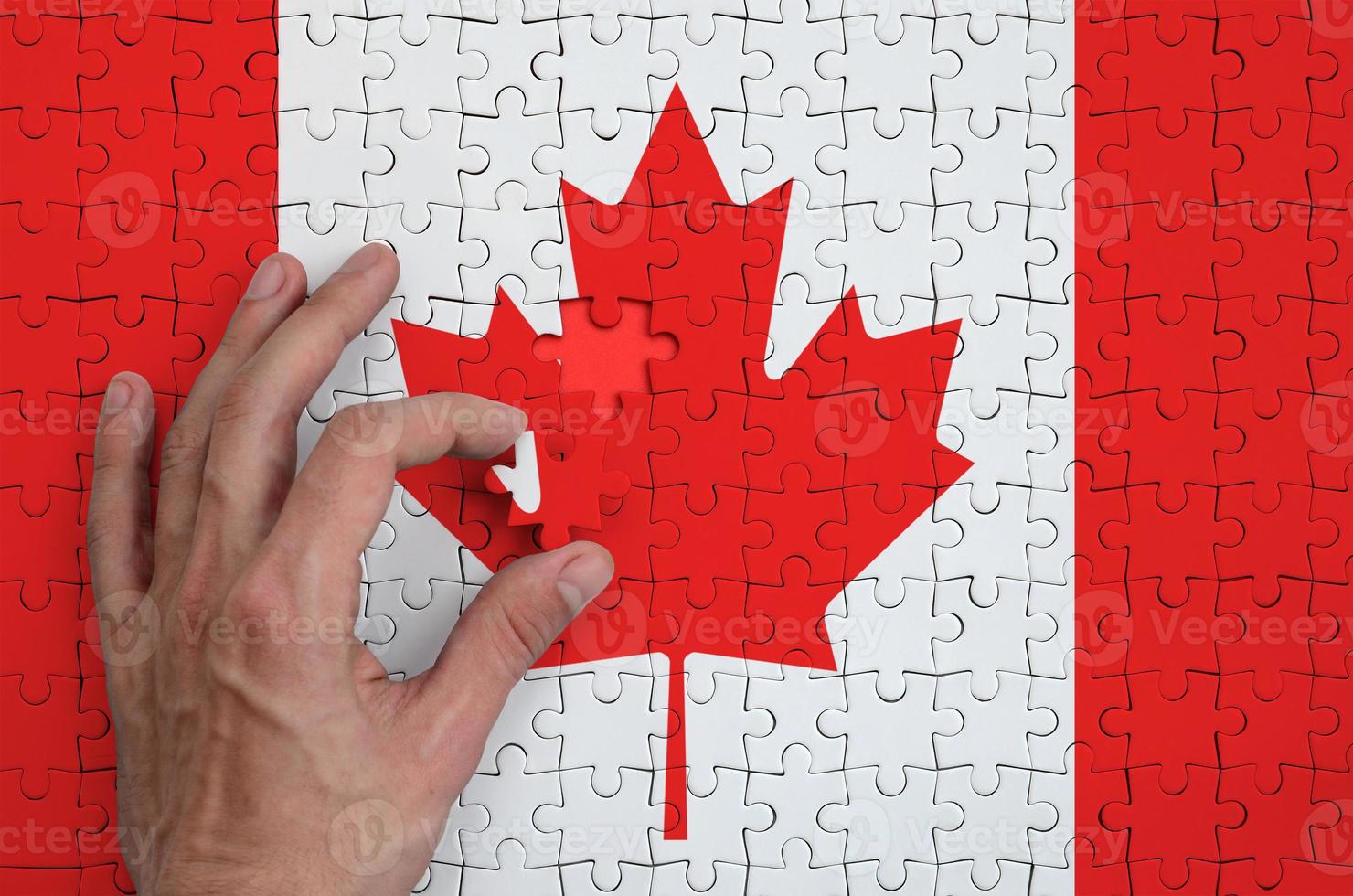 Canada flag is depicted on a puzzle, which the man's hand completes to fold photo