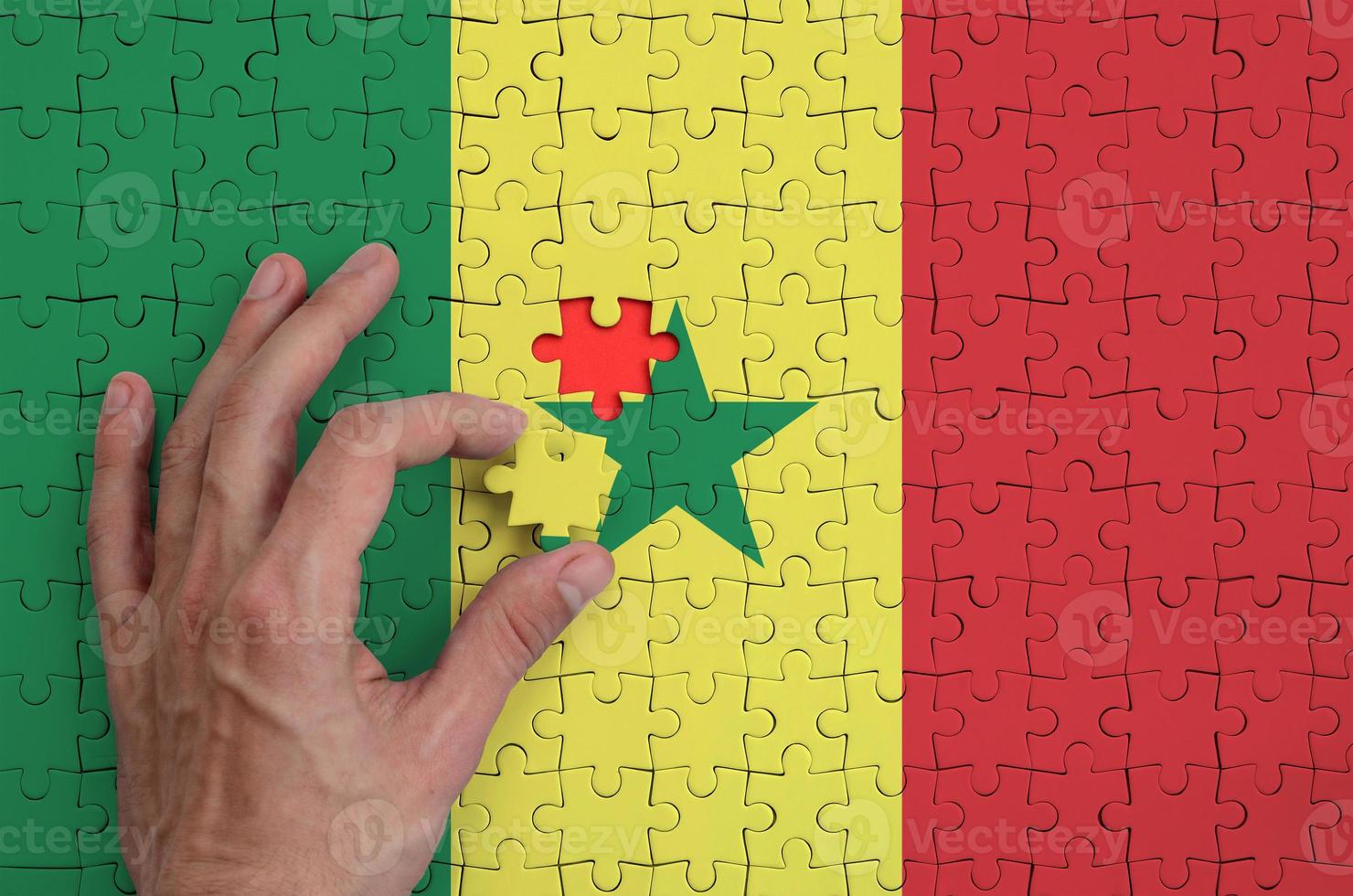 Senegal flag is depicted on a puzzle, which the man's hand completes to fold photo