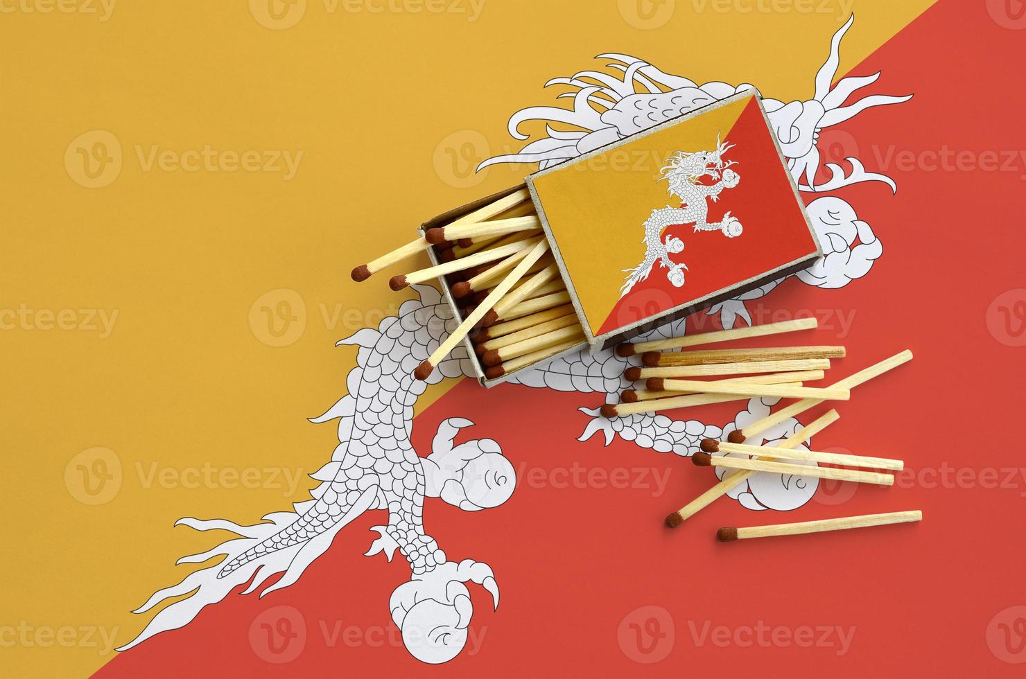 Bhutan flag is shown on an open matchbox, from which several matches fall and lies on a large flag photo