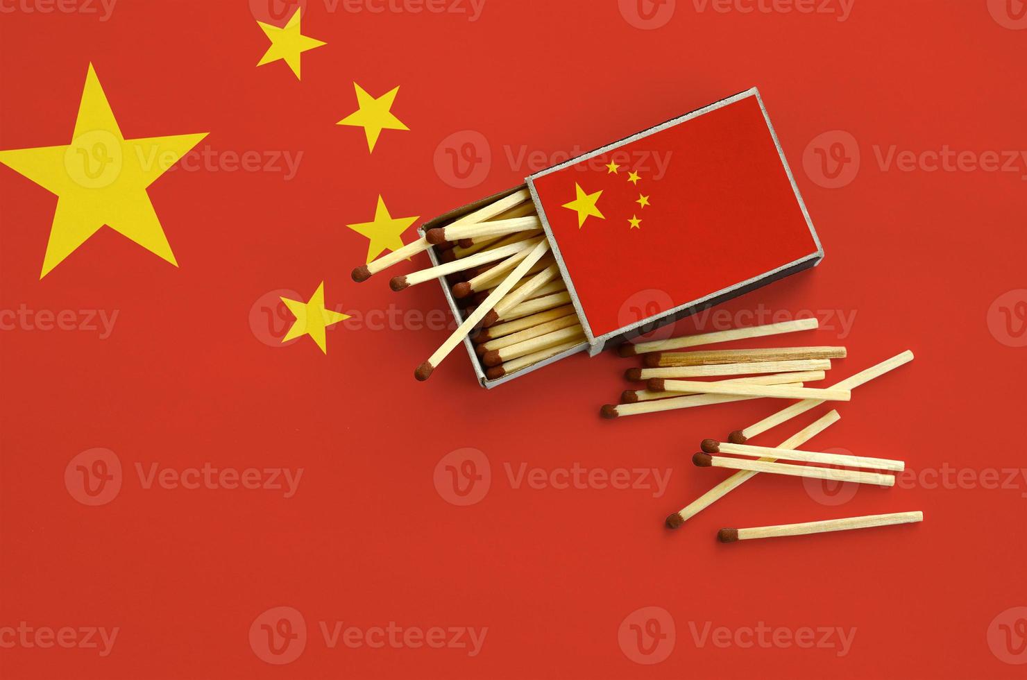 China flag is shown on an open matchbox, from which several matches fall and lies on a large flag photo