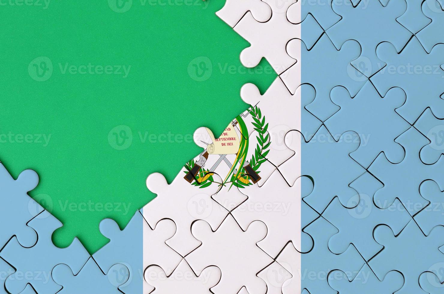 Guatemala flag is depicted on a completed jigsaw puzzle with free green copy space on the left side photo