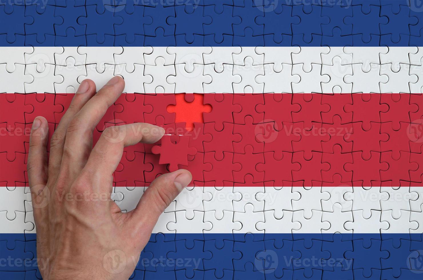 Costa Rica flag is depicted on a puzzle, which the man's hand completes to fold photo