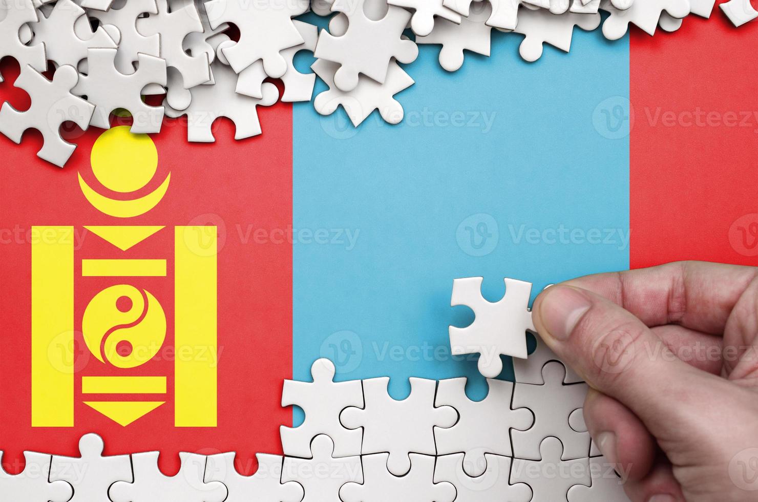Mongolia flag is depicted on a table on which the human hand folds a puzzle of white color photo