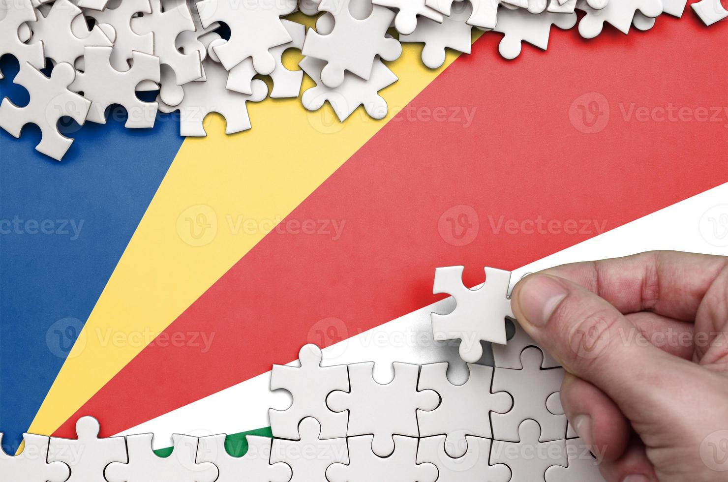 Seychelles flag is depicted on a table on which the human hand folds a puzzle of white color photo