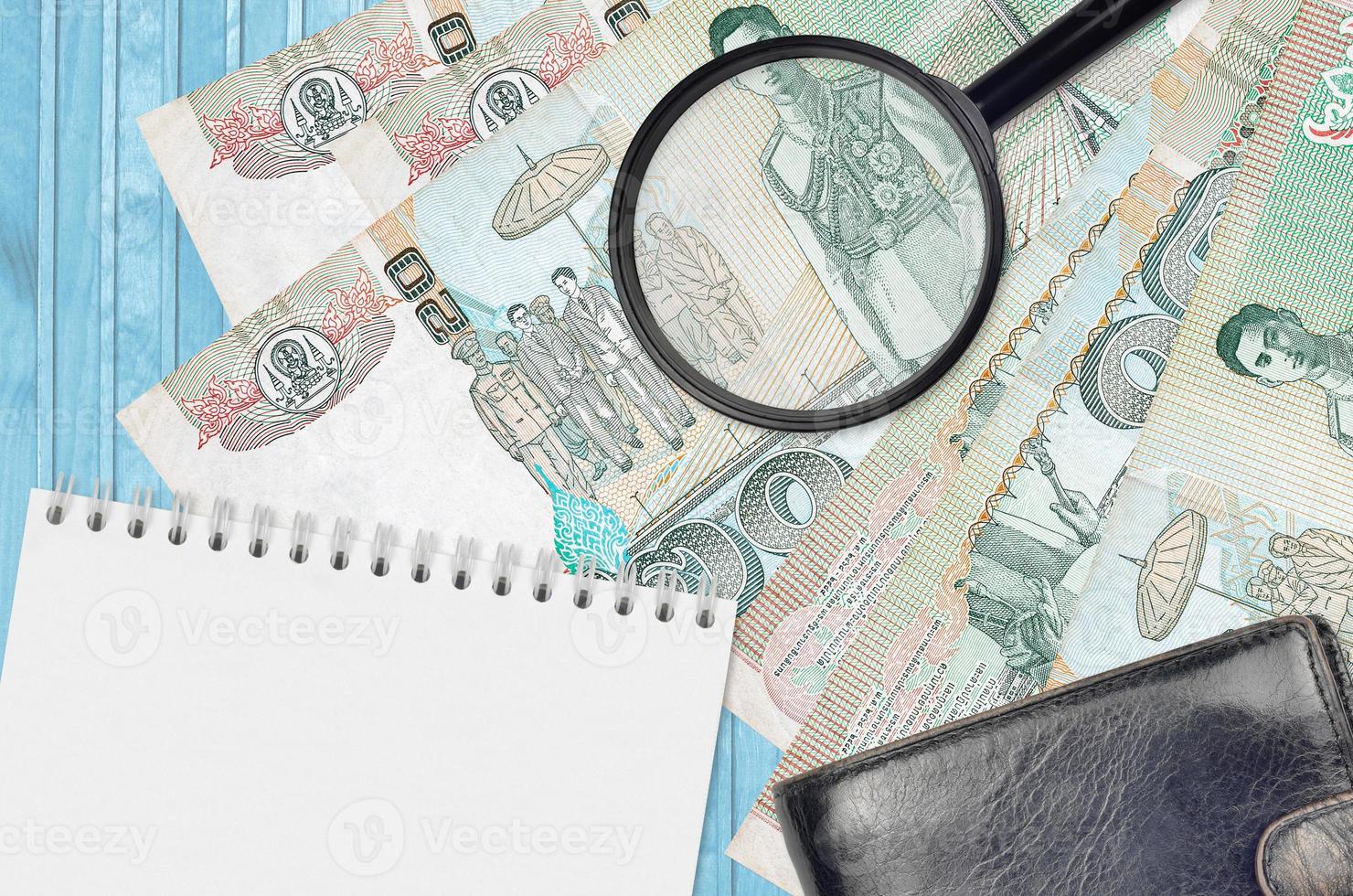 20 Thai Baht bills and magnifying glass with black purse and notepad. Concept of counterfeit money. Search for differences in details on money bills to detect fake photo