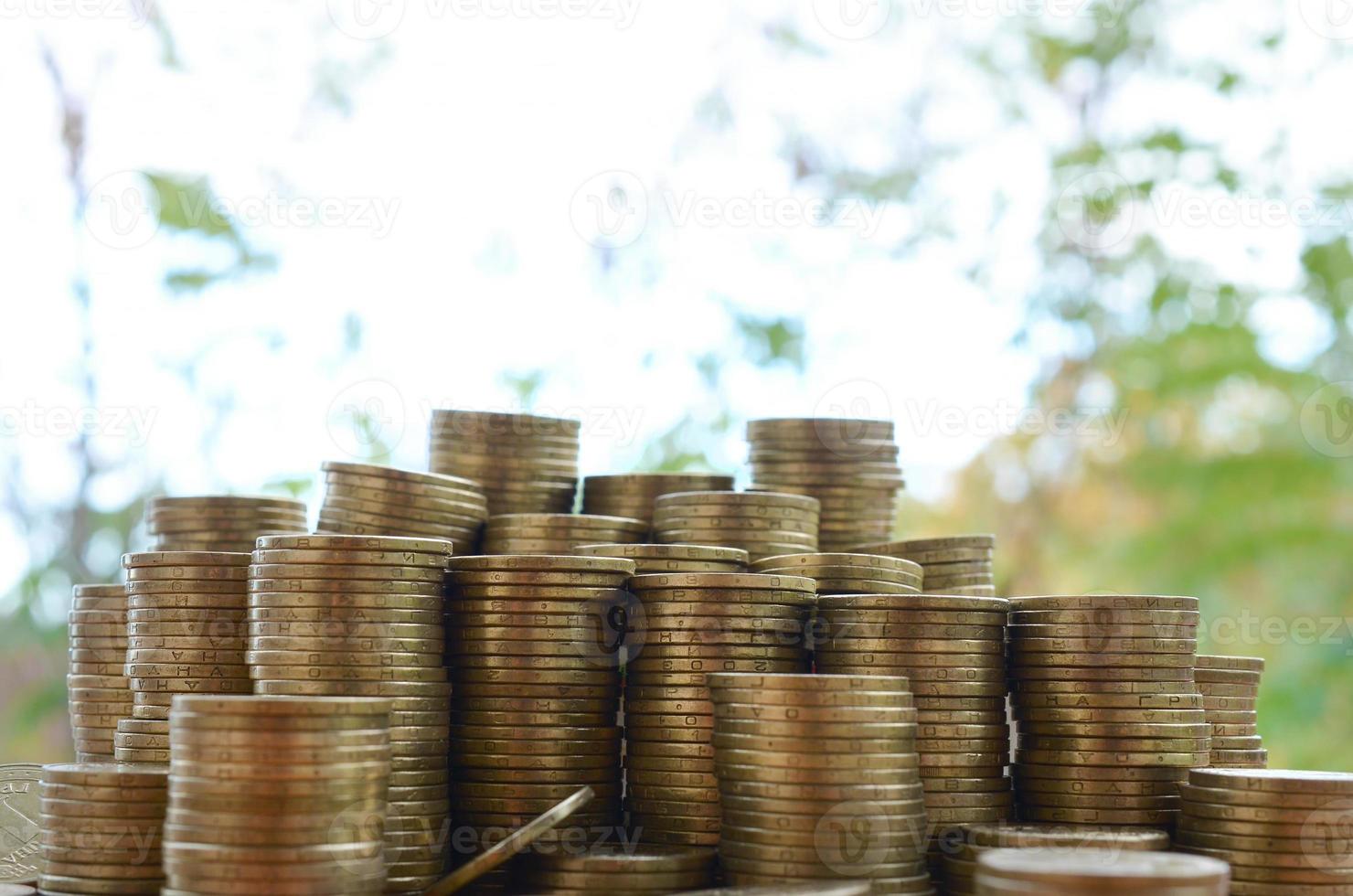 Big amount of shiny ukrainian old 1 hryvnia coin stacks close up on wooden table on green trees backdrop. The concept of business and rich life in Ukraine photo