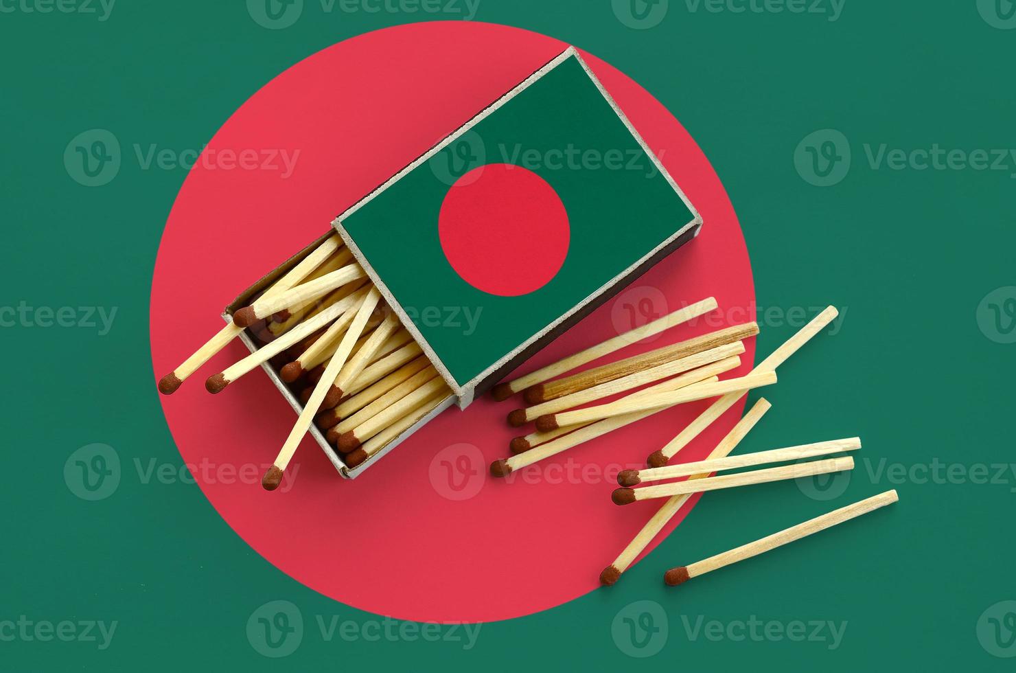 Bangladesh flag is shown on an open matchbox, from which several matches fall and lies on a large flag photo