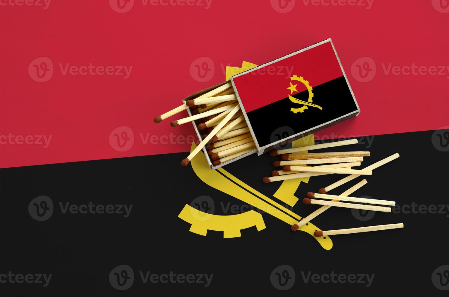 Angola flag is shown on an open matchbox, from which several matches fall and lies on a large flag photo