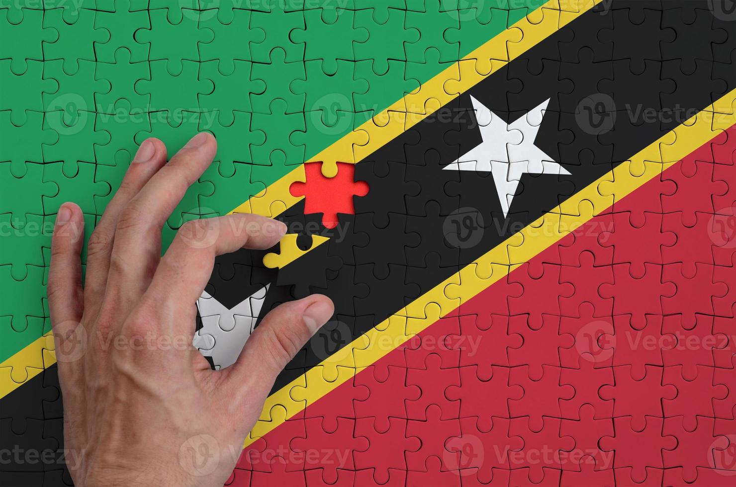Saint Kitts and Nevis flag is depicted on a puzzle, which the man's hand completes to fold photo