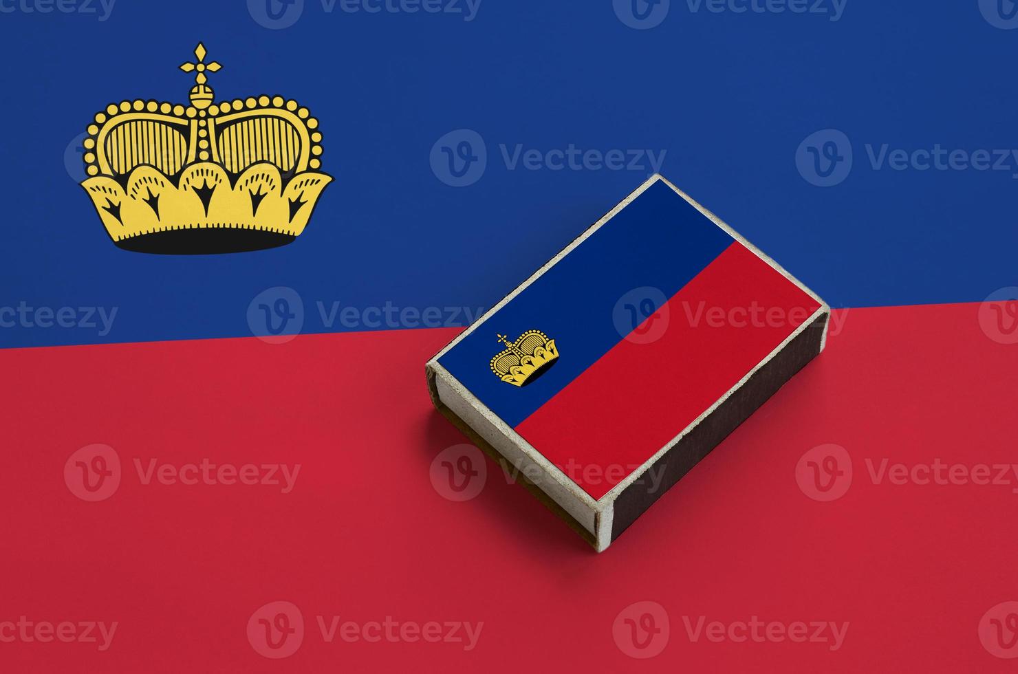 Liechtenstein flag is pictured on a matchbox that lies on a large flag photo
