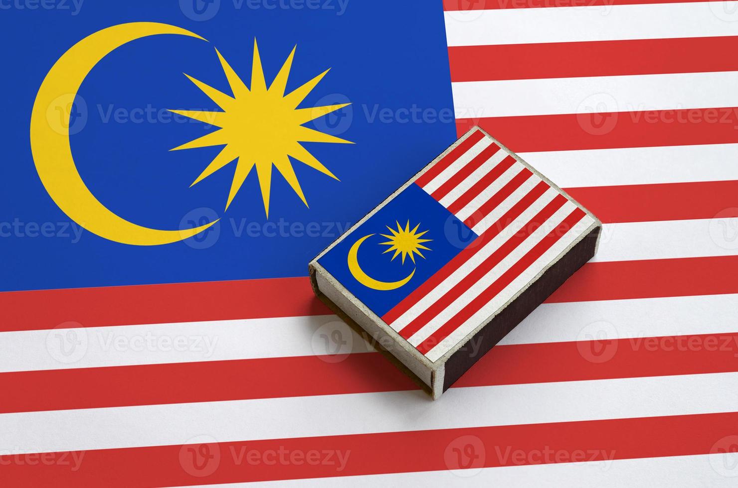 Malaysia flag is pictured on a matchbox that lies on a large flag photo