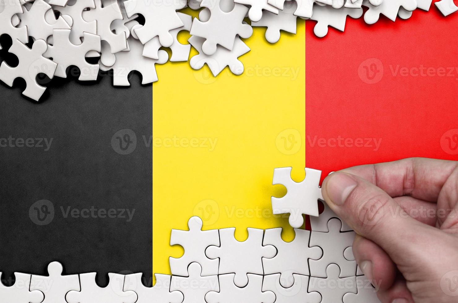 Belgium flag is depicted on a table on which the human hand folds a puzzle of white color photo