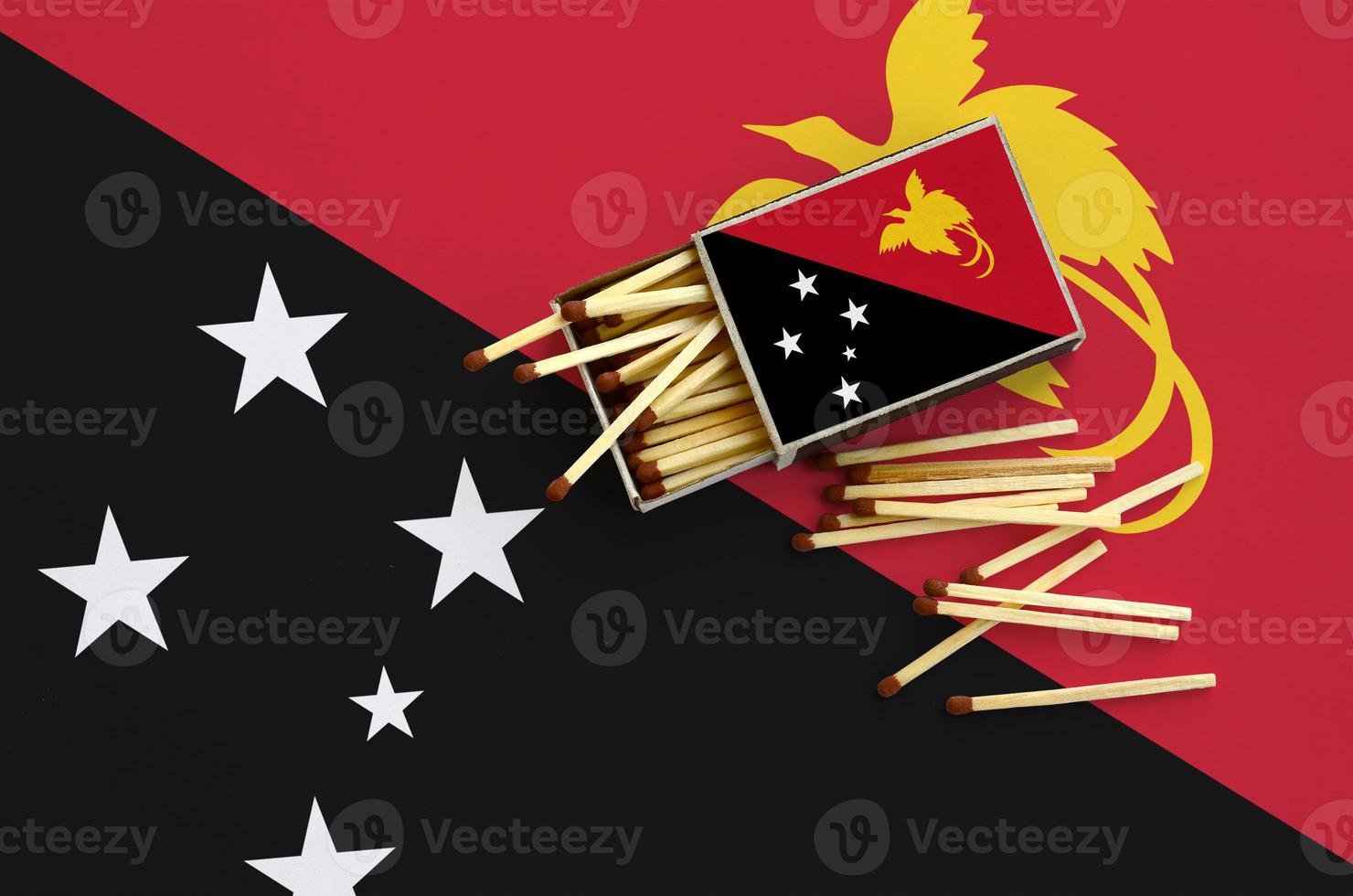 Papua New Guinea flag is shown on an open matchbox, from which several matches fall and lies on a large flag photo