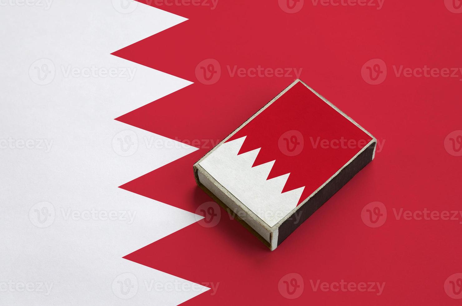 Bahrain flag is pictured on a matchbox that lies on a large flag photo