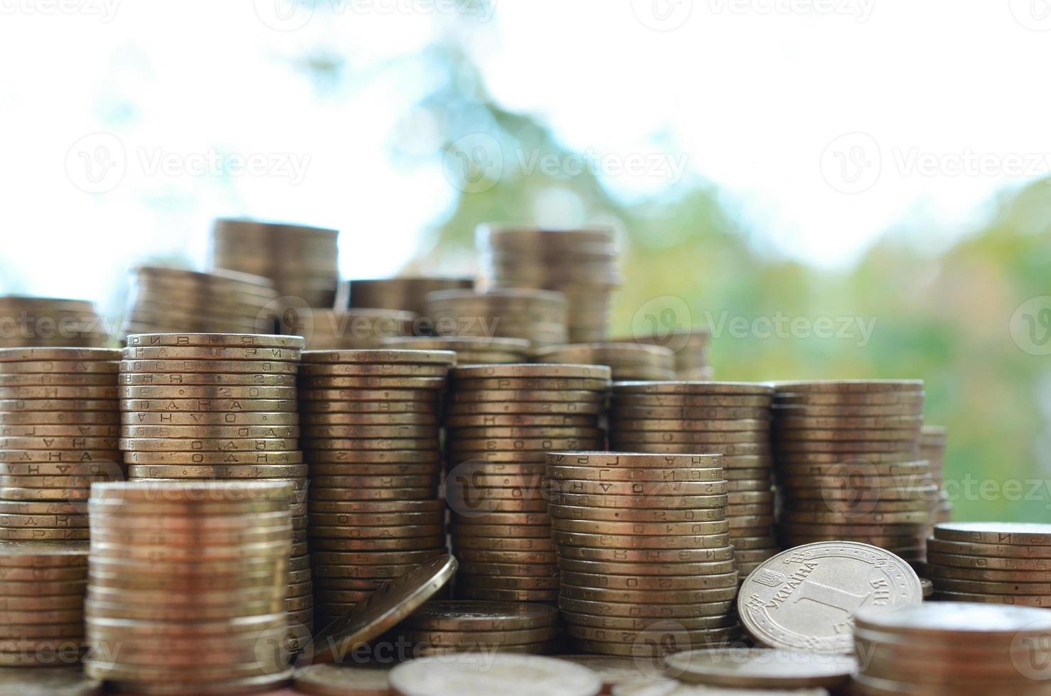 Big amount of shiny ukrainian old 1 hryvnia coin stacks close up on wooden table on green trees backdrop. The concept of business and rich life in Ukraine photo