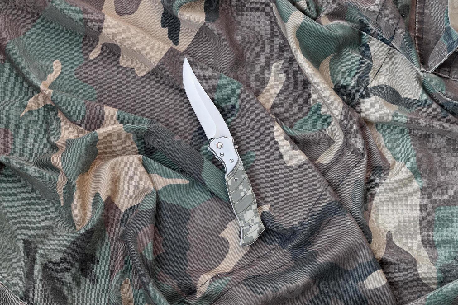 Military knife on army camouflage clothes close up. Background with copy space for military or special service design photo