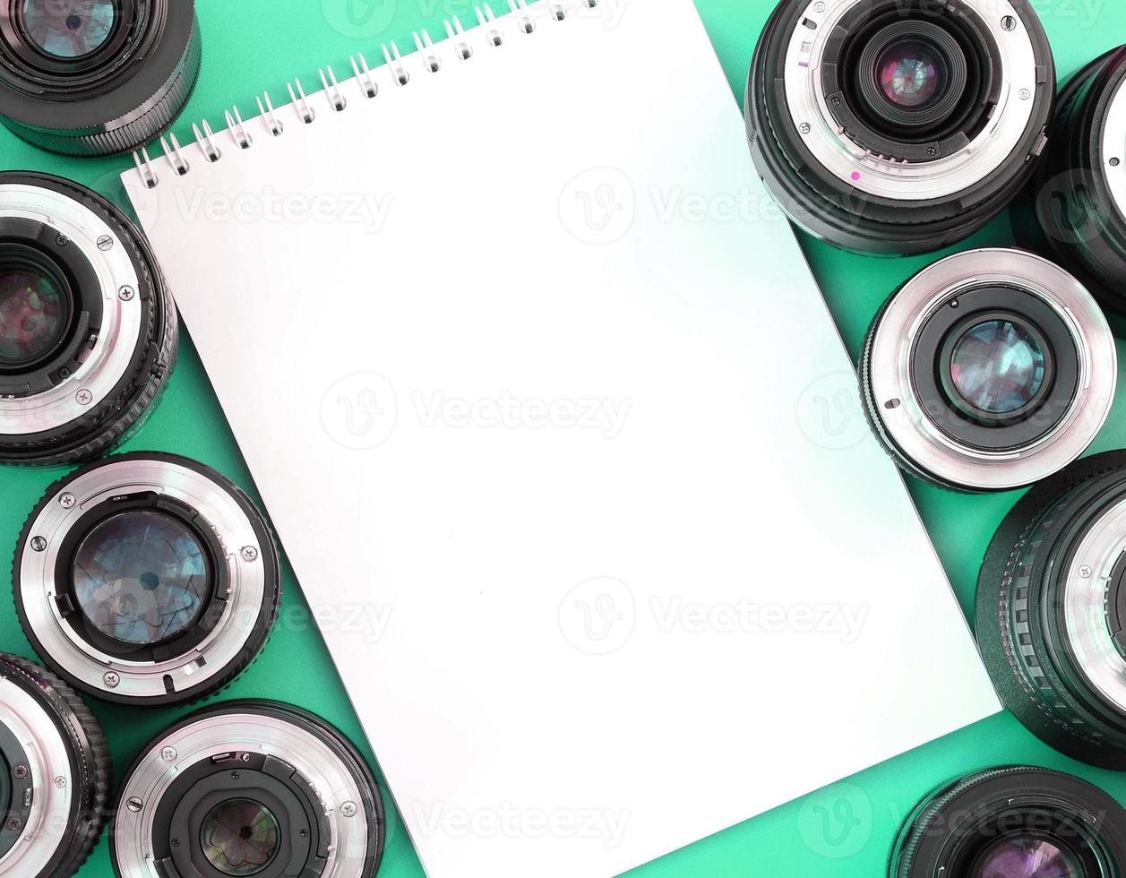 Several photographic lenses and white notebook lie on a bright turquoise background. Copy space photo