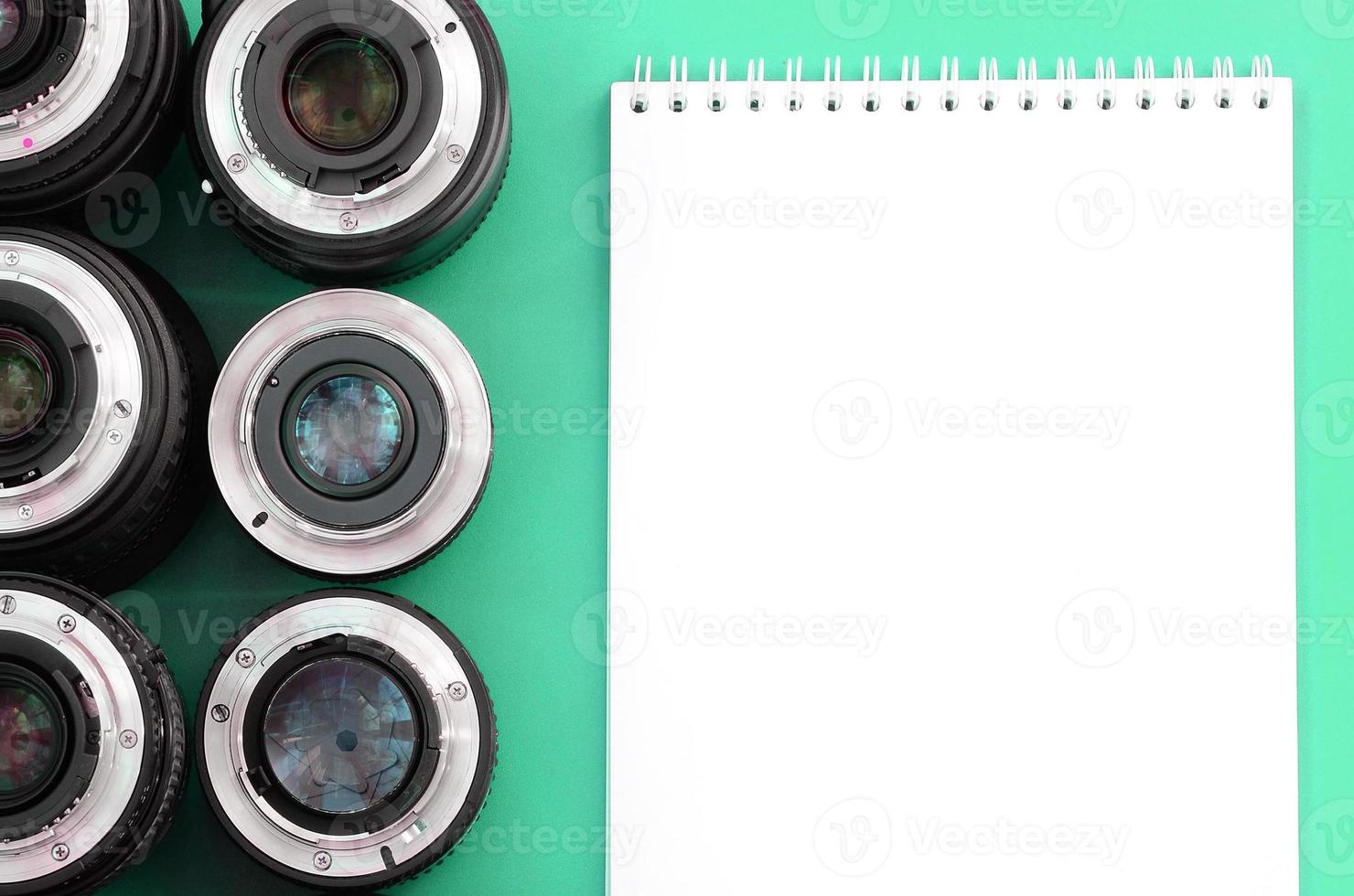 Several photographic lenses and white notebook lie on a bright turquoise background. Copy space photo