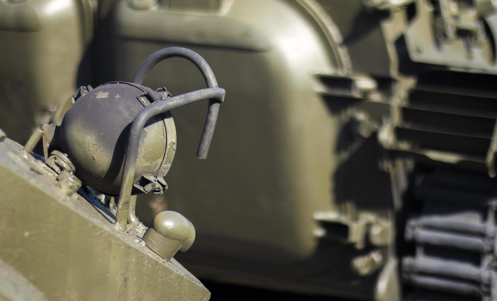 Front headlight with battle tank protection. Very bright searchlight on the tank turret, close-up. Armored infantry fighting vehicle. Fragment of an old armored personnel carrier, khaki headlight. photo