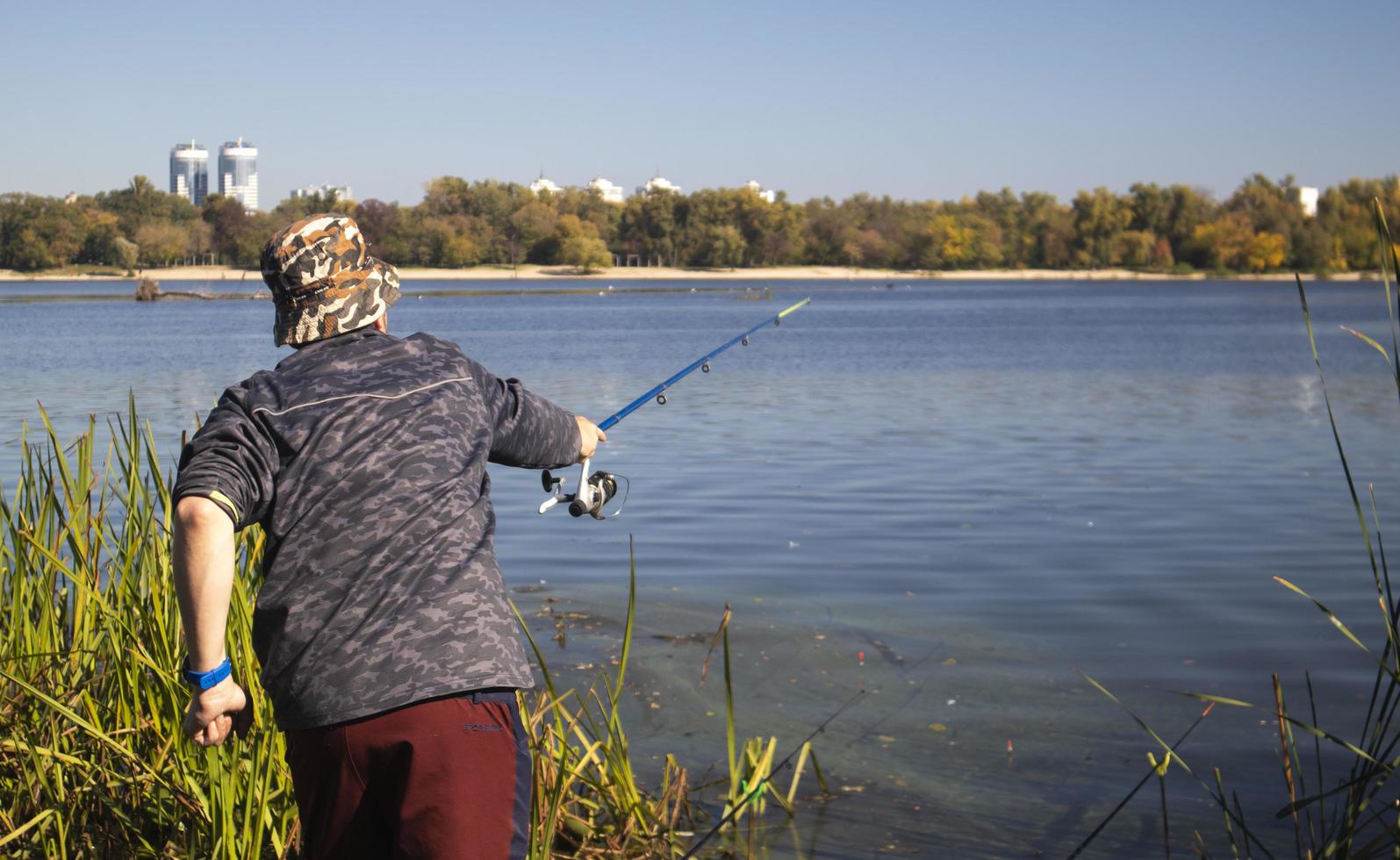 A male fisherman threw a spinning rod into a lake or river on a sunny day. Shore fishing. A fisherman on the river bank holds a spinning rod in his hand. The concept of country rest. Fishing article. photo