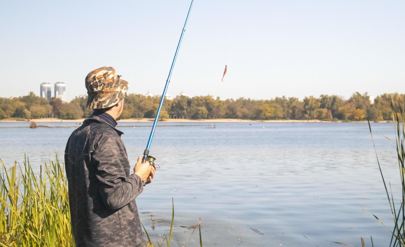 A male fisherman threw a spinning rod into a lake or river on a sunny day. Shore fishing. A fisherman on the river bank holds a spinning rod in his hand. The concept of country rest. Fishing article. photo