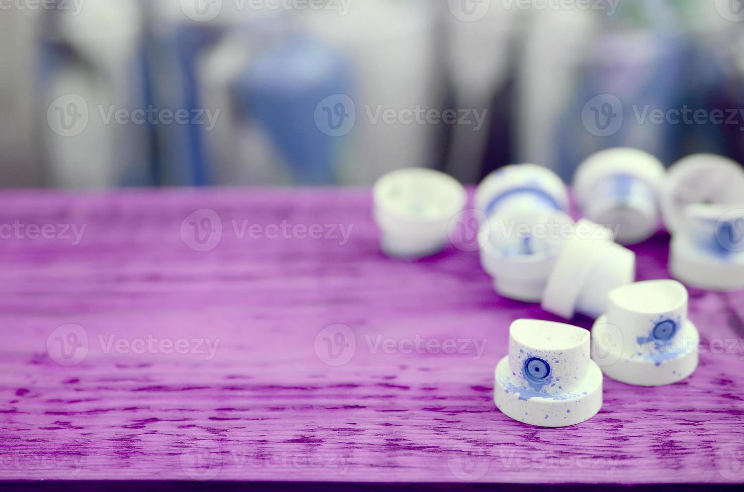 The soiled blue nozzles from the paint sprayer lies on a purple plank on a background of a many dirty spray cans photo