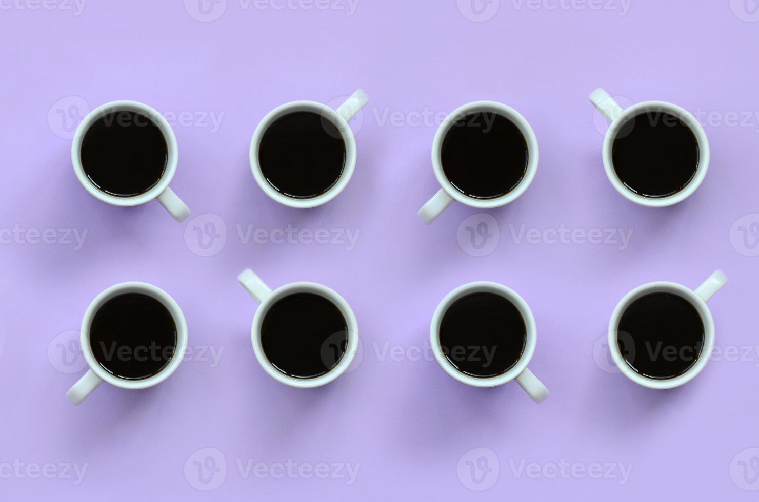 muchas tazas pequeñas de café blanco sobre fondo de textura de papel de color violeta pastel de moda en concepto mínimo foto