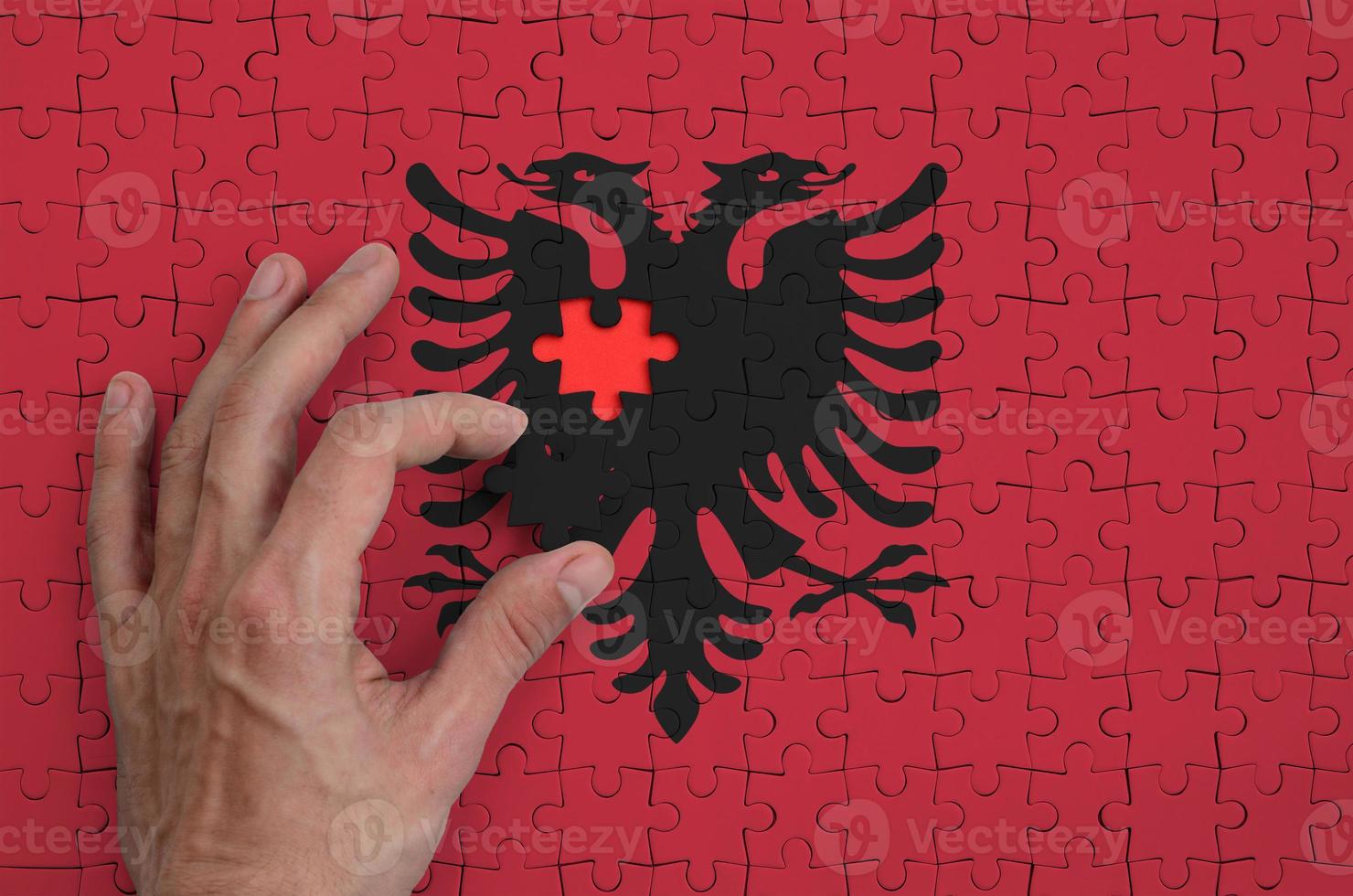 Albania flag is depicted on a puzzle, which the man's hand completes to fold photo