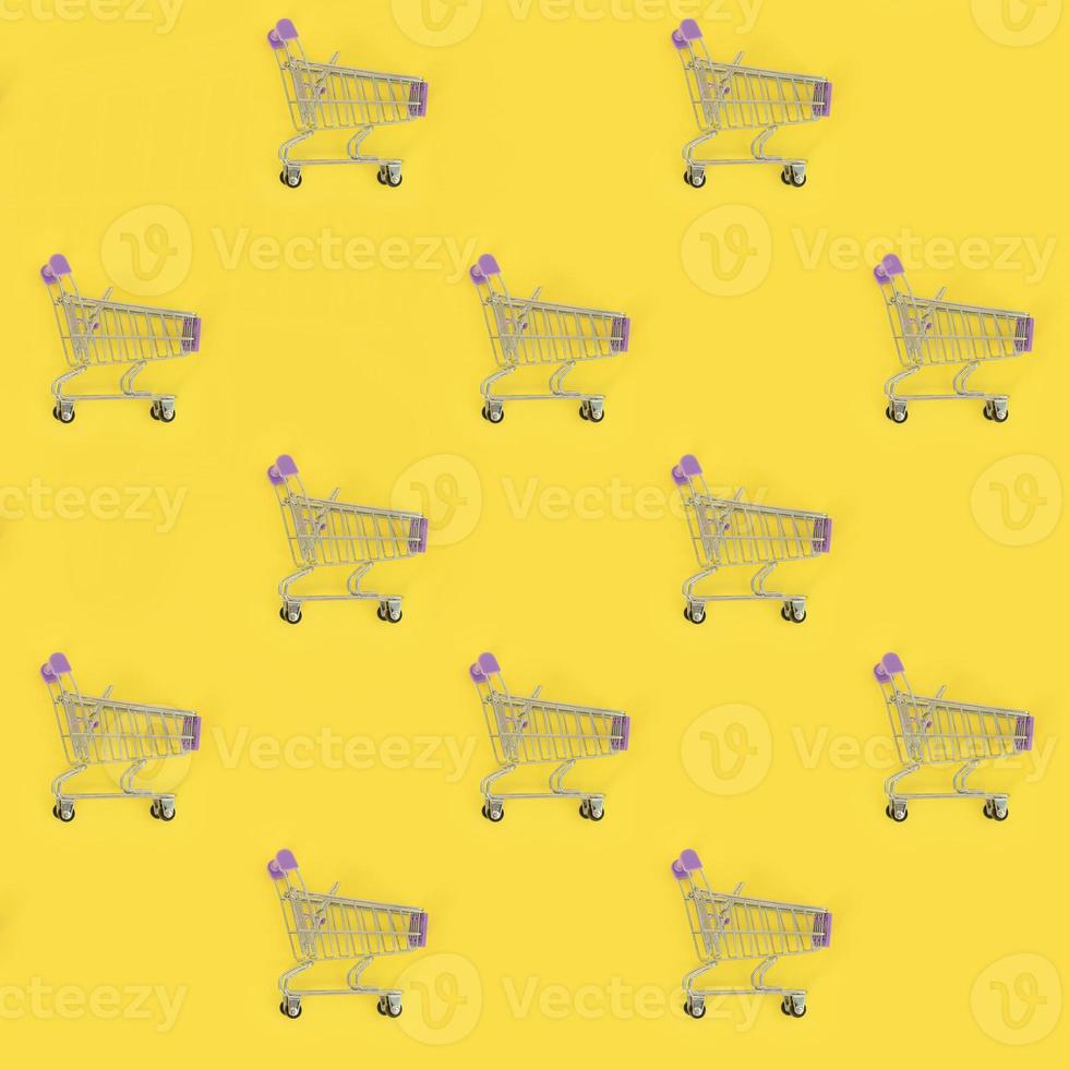 Shopping addiction, shopping lover or shopaholic concept. Many small empty shopping carts perform a pattern on a pastel colored paper background. Flat lay composition, top view photo