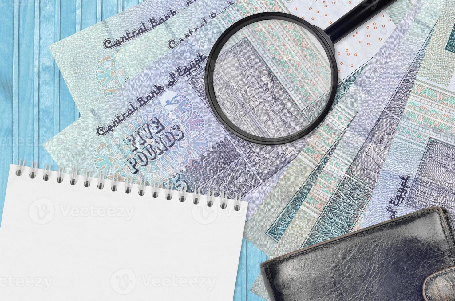 5 Egyptian pounds bills and magnifying glass with black purse and notepad. Concept of counterfeit money. Search for differences in details on money bills to detect fake photo