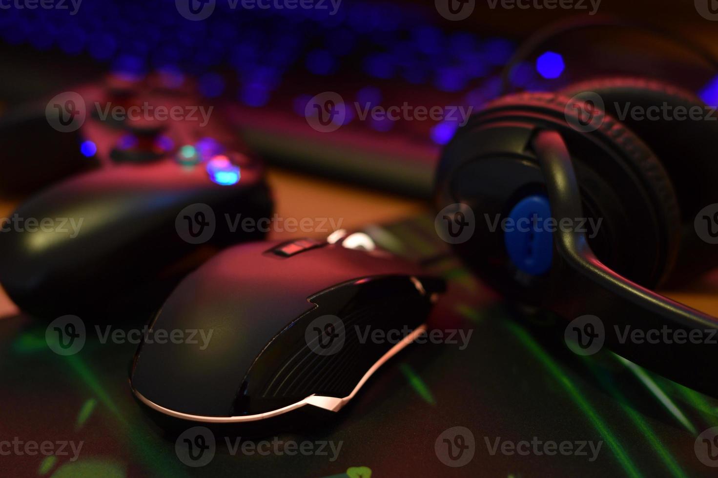 Modern gamepad and gaming mouse lies with keyboard and headphones on table in dark playroom scene. Gameplay streaming and video game walkthroughts concept photo