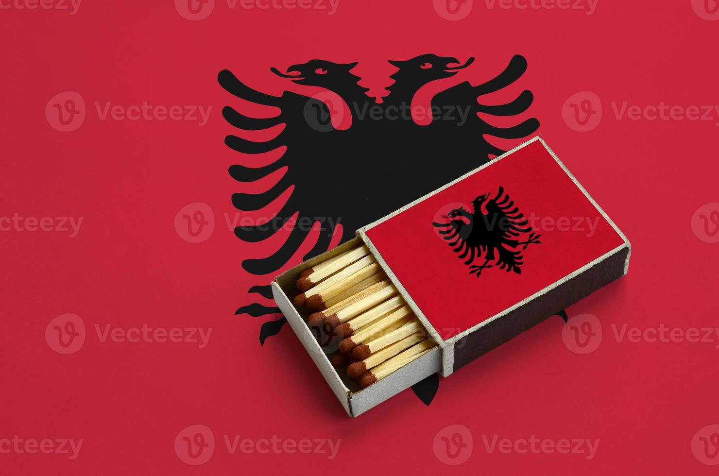 Albania flag is shown in an open matchbox, which is filled with matches and lies on a large flag photo